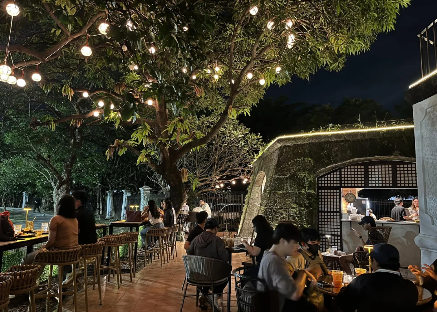 Guests at outdoor café tables beneath a tree and hanging lights at Café Y Ruedas.